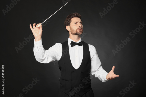 Professional conductor with baton on black background