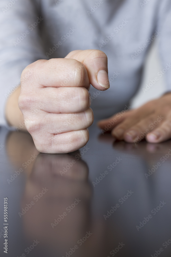 Woman hand with clenched fist hitting table expressing power, anger or stop it, on dark table with reflection