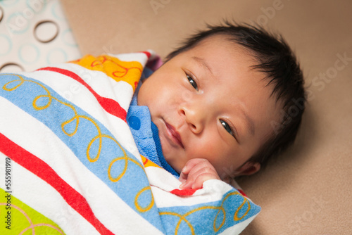 Close-up portrait of two week old, newborn Asian baby girl, wrapped in colorful swaddling blanket, studio shot photo