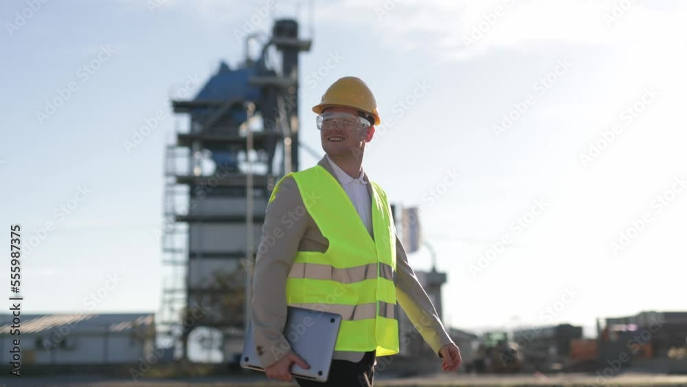 A professional engineer, a heavy industry worker, an inspector dressed in a protective uniform and a helmet, carries a tablet computer. A smiling industrial specialist strolling through the production A professional engineer, a heavy industry worker, an inspector dressed in a protective uniform and a helmet, carries a tablet computer. A smiling industrial specialist strolling through the production