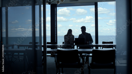 Business team silhouettes talking at sea clouds view. Two managers work laptop
