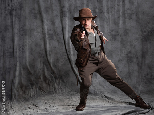 A young man in retro style, an adventure character. The hero of the adventure, a guy in a hat and a leather jacket, shoots a pistol in a spectacular lunge