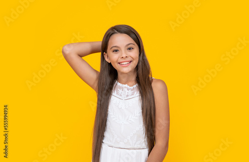 positive teen girl in white dress has long hair on yellow background
