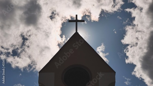 The silhouette of a Catholic church tower against a background of sun and clouds.