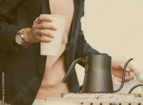 A hand of barista catch a  white coffee cup .There is a kettle on the table. , close up shot .Coffee shop concept.