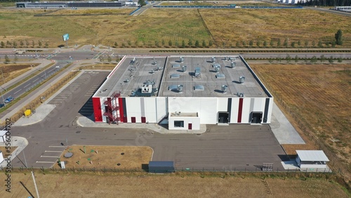 Industrial building of a plant for the manufacture of medical equipment. The gray roof of a modern industrial building standing in a field. White-red facade of a medical plant.