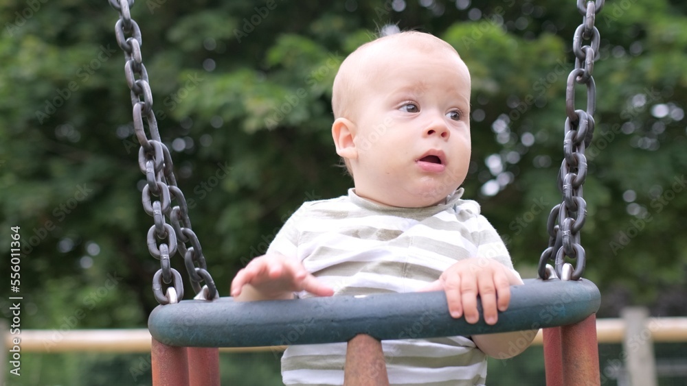 Funny Little Younger Newborn Infant Brother Boy On Swing. Baby Playing On Playground. Summer time outside. Kids Entertainment, Childhood, Child Development, Happy Family Concept