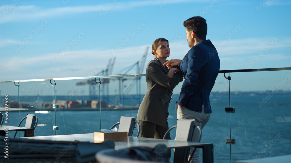 Financial managers discussing project on glass balcony in golden sunlight.