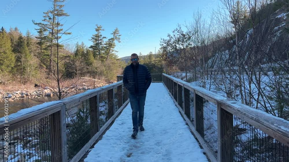 Man walking across a snowy bridge over a river at winter - slow motion Man walking across a snowy bridge over a river at winter - slow motion
