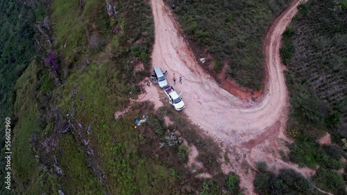 Pickup truck cars parked on dirt road bend and people waving hat greeting drone flying overhead in Cajamarca mountainous region in Peru. Aerial orbiting overhead photo