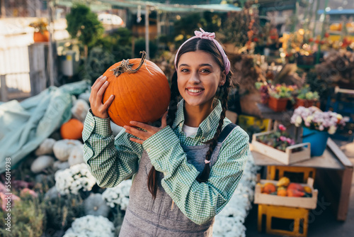 Happy farmer woman in a denim jumpsuit holds ripe pumpkin