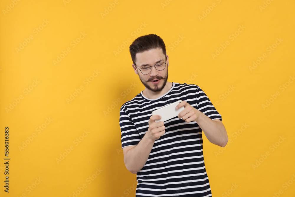 Emotional man playing game on phone against orange background Emotional man playing game on phone against orange background