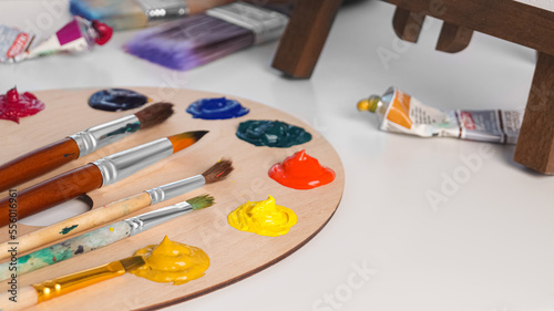 Artist's palette with samples of colorful paints and brushes on white table. Space for text