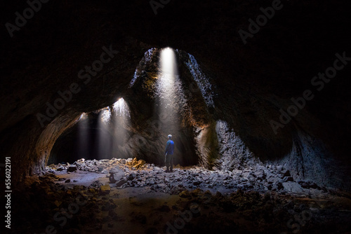 Adventurous athletic male standing in a lava tube looking at the sunlight shinning down into the cave through holes in the ceiling.
