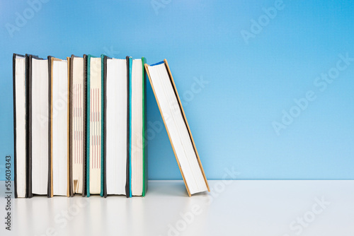 Stack of books in the colored cover lay on the wooden table and blue backround. Education learning concept