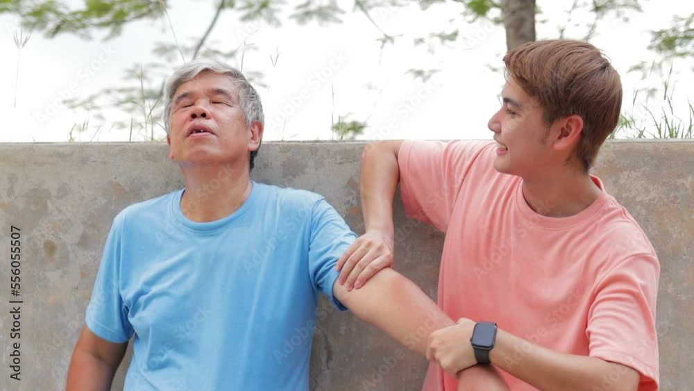 Asian father and son exercising outdoors together Standing to rest, grandson massages the arm of an elderly man. Sport concept, healthy exercise. family activities Asian father and son exercising outdoors together Standing to rest, grandson massages the arm of an elderly man. Sport concept, healthy exercise. family activities