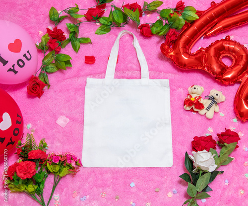 White blank tote bag on the top of a fluffy pink carpet surrounded by valentine themed decorations