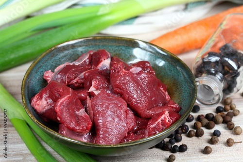 Raw deer meat for venison ragout or goulash. Bowl with pieces of deer meat, fresh vegetable, juniper berries and allspice for cooking around.