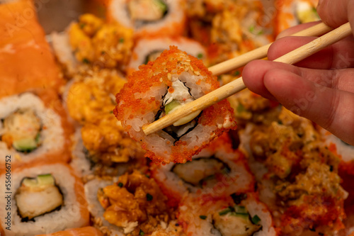 Someone takes a chopsticks roll from a set of different types of rolls in a box.