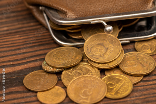 Old coins of the USSR and a vintage wallet made of brown leather on a wooden surface.