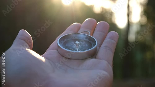 Compass in hand on natural pine forest background. hand holding compass in forest landscape. Young traveler searching direction with compass in summer mountains.