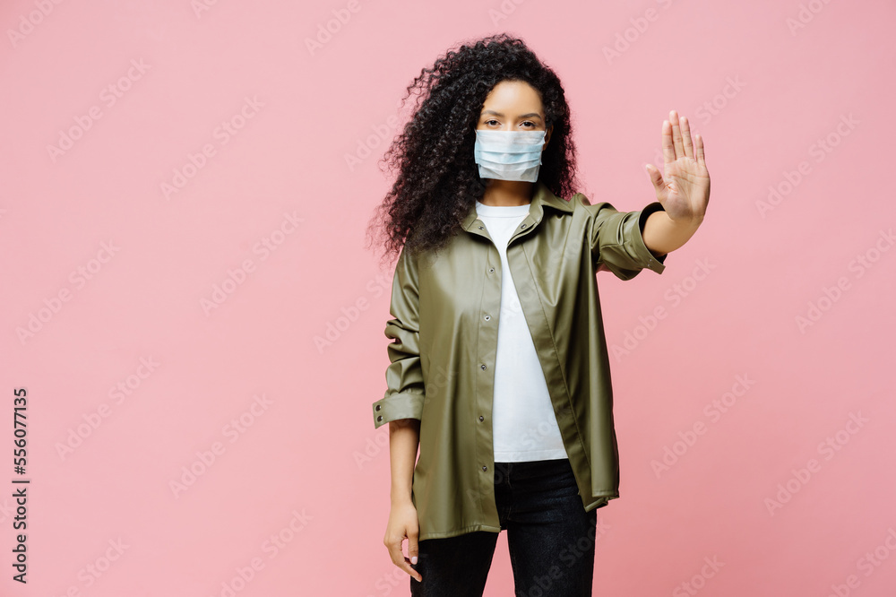 Horizontal shot of Afro American woman keeps palm towards camera, makes stop gesture, tries to prevent coronavirus or Covid-19, wears protective sterile mask, says no to world pandemic disease Horizontal shot of Afro American woman keeps palm towards camera, makes stop gesture, tries to prevent coronavirus or Covid-19, wears protective sterile mask, says no to world pandemic disease