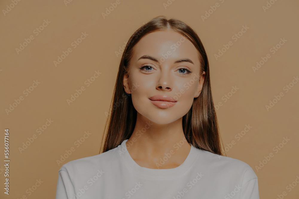 Portrait of pretty European woman with long hair looks confidently ar camera has healthy glowing skin makeup wears casual jumper isolated over brown studio wall. Beauty and wellness concept. Portrait of pretty European woman with long hair looks confidently ar camera has healthy glowing skin makeup wears casual jumper isolated over brown studio wall. Beauty and wellness concept.
