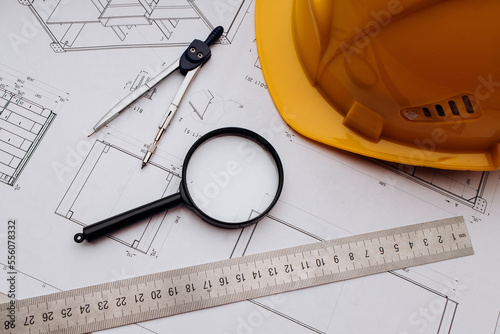 Blueprint, magnifier and yellow safety helmet on workplace desk