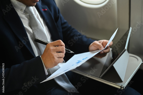 Cropped shot of businessman reading financial document with tablet on foreground while sitting in airplane cabin