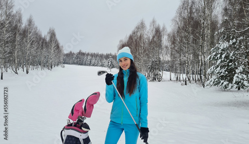 Beautiful female golfer holds a golf club in winter on golf course
