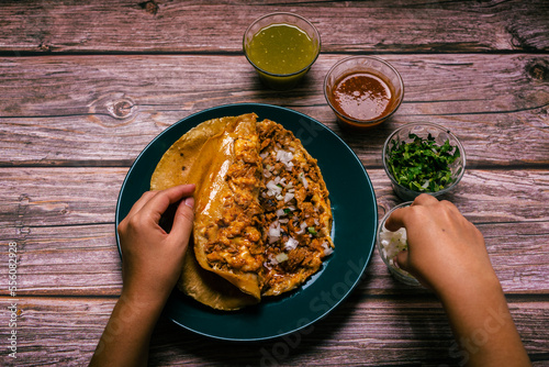 Hands of a person preparing a gringa pastor a la diabla accompanied by sauces and other condiments on a wooden table. Gringa, typical Mexican dish. photo