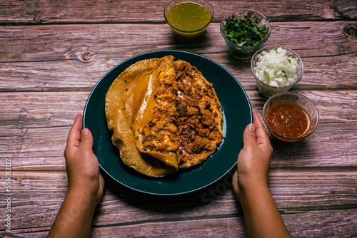 Hands of a person preparing a gringa pastor a la diabla accompanied by sauces and other condiments on a wooden table. Gringa, typical Mexican dish. photo