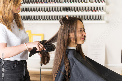 The hairdresser dries the client's hair with a hair dryer and styles her hair with a comb.