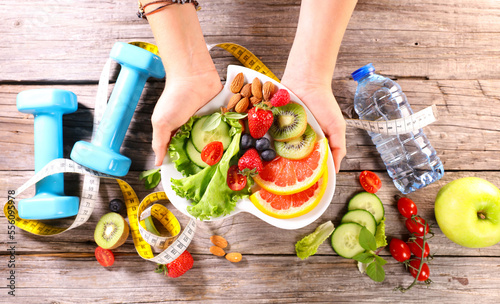 healthy eating concept- hand holding plate with fresh vegetables, dumbell, apple and water- sport health food