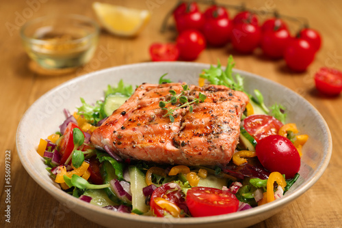 Bowl with tasty salmon and mixed vegetables on wooden table, closeup