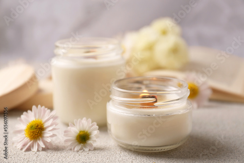 Obraz na plátne Burning scented candles and chamomile flowers on light gray textured table, closeup