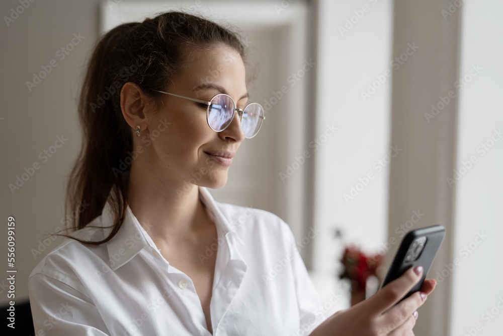 A woman with glasses writes a message on her phone. A close portrait with glasses, working in an office.