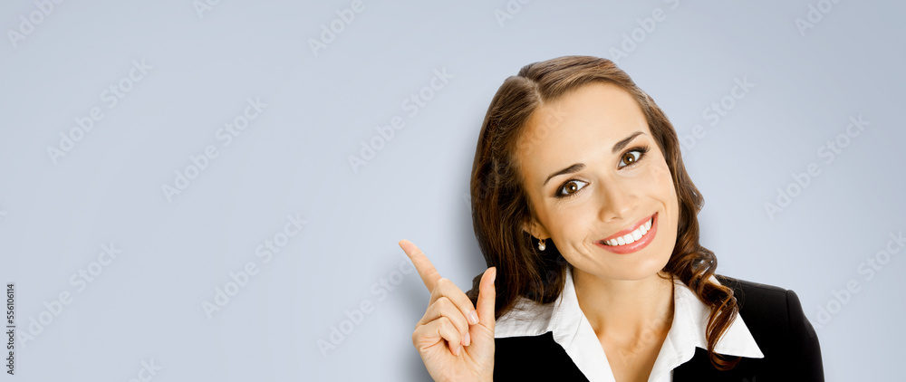 Obraz premium Portrait of amazed smiling woman in black confident suit, pointing showing indicating copy space. Business concept. Brunette businesswoman. Gray color background