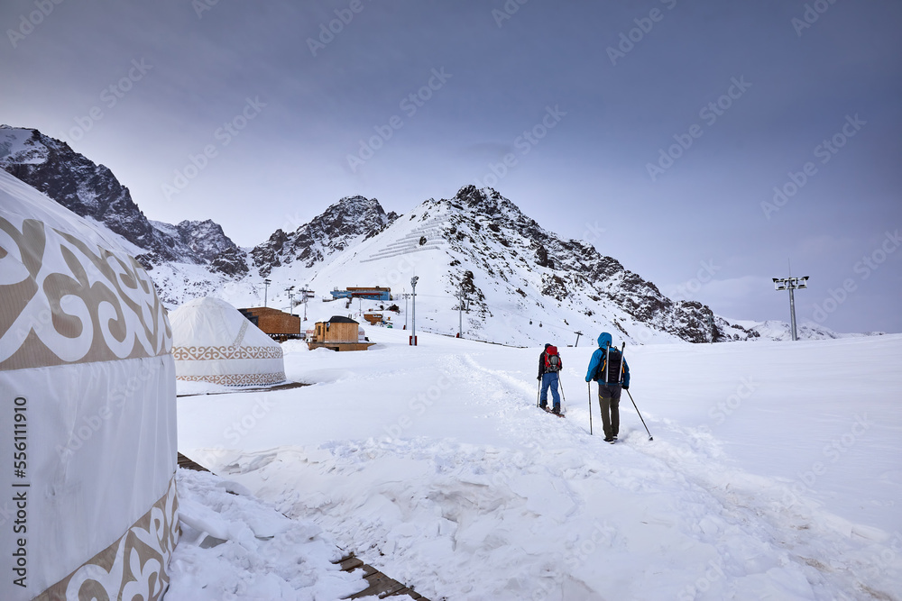 Two men skiing near yurt house snowy mountains