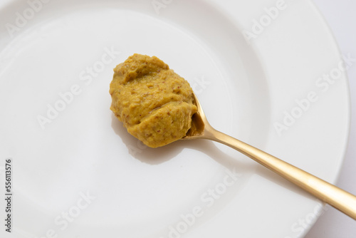 Dijon mustard spoon on white plate on white background. Hot sauce on golden spoon