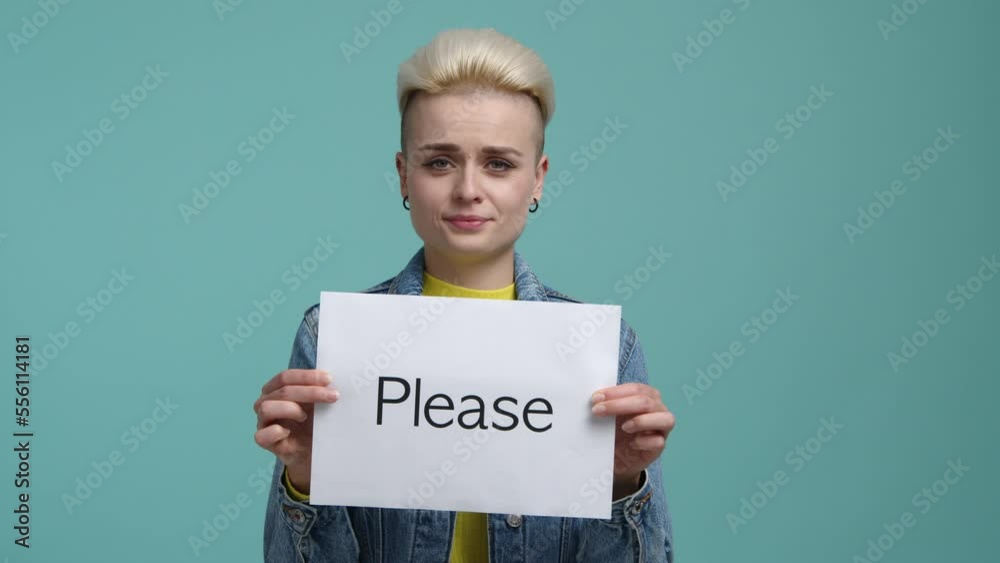 Blonde-haired woman holding a card with a Please word. Portrait of stylish, caucasian girl with a praying facial expression. High quality 4k footage Blonde-haired woman holding a card with a Please word. Portrait of stylish, caucasian girl with a praying facial expression. High quality 4k footage