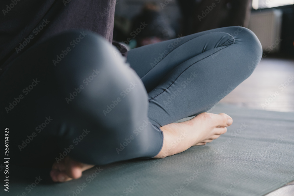 Naklejka premium Close-up photo of the legs of a female yogi meditating barefoot and wearing leggings in easy pose on a yoga mat on the floor