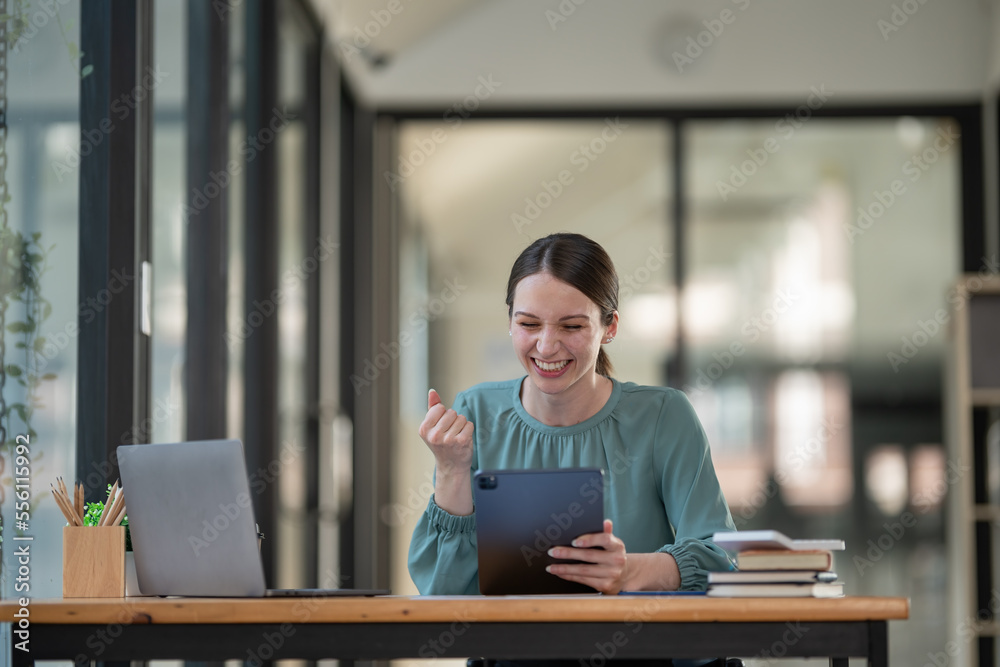 Cheerful businesswoman celebrating her achievement while reading good news on a digital tablet from the office. Cheerful businesswoman celebrating her achievement while reading good news on a digital tablet from the office.