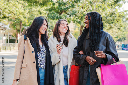 Three multiracial happy young women walking and talking on a shopping day. Group of girls carrying bags smiling on the street on a sale week. Consumism concept. High quality photo photo