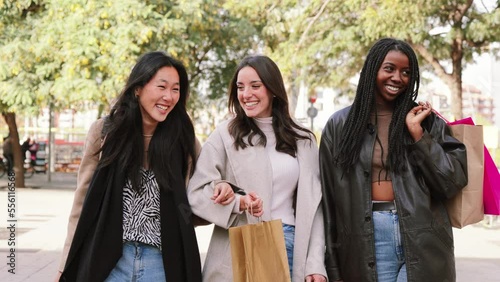 Three multiracial happy young women walking and talking on a shopping day. Group of girls carrying bags smiling on the street on a sale week. Consumism concept. High quality photo photo