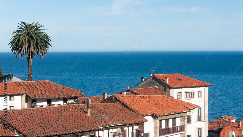 Tejados de teja de arcilla en pueblo marinero de Asturias junto a horizonte marino