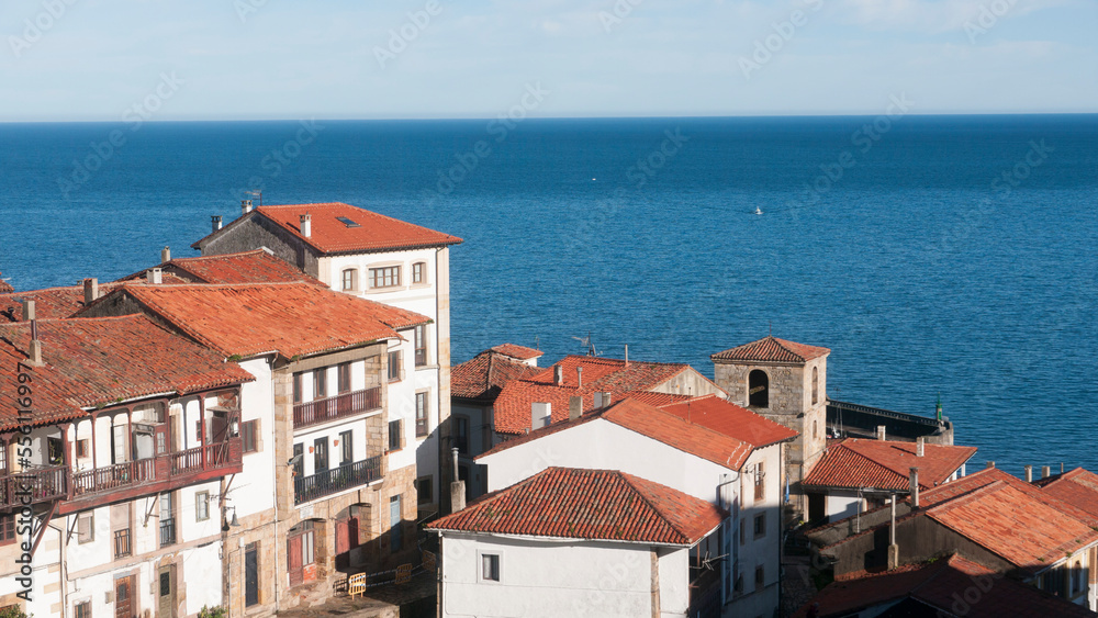 Tejados de teja de arcilla en pueblo marinero de Asturias junto a horizonte marino