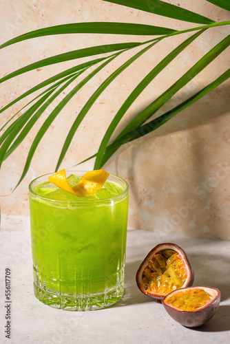 Tropical fruit cocktail in sunshine on stone background with palm leaves. Green juice shake. Gin drink with passion and mango liqueur. Refreshing alcoholic beverage at the beach bar. Copy space