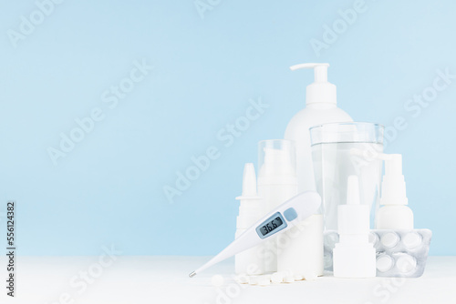 Medical and treatment background with white bottles mockup for prevent and teraphy disease and sickness, health - 36,6 thermometer, sprays, salves, pills on white table, blue wall, copy space. photo