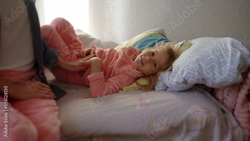 The child is lying on the bed, the mother is stroking her stomach. The child has a stomach ache, the mother's hands caress it. 
Mom is caressing the child.